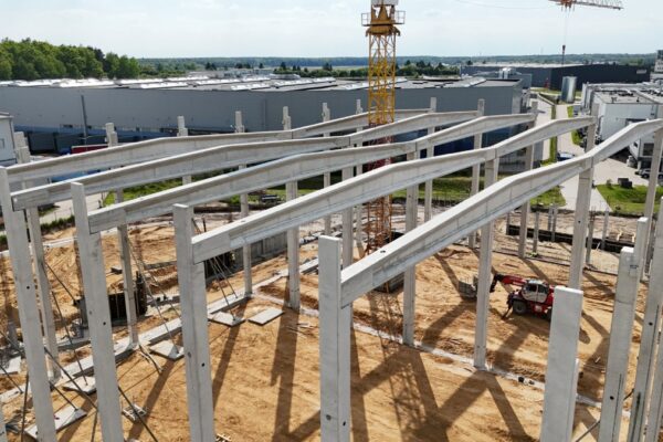 Rząd dźwigarów dachowych na słupach hali, w tle żuraw wieżowy