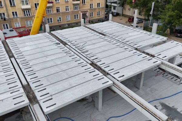 Ułożone płyty kanałowe na belkach, w tle kamienica i ramię dźwigu